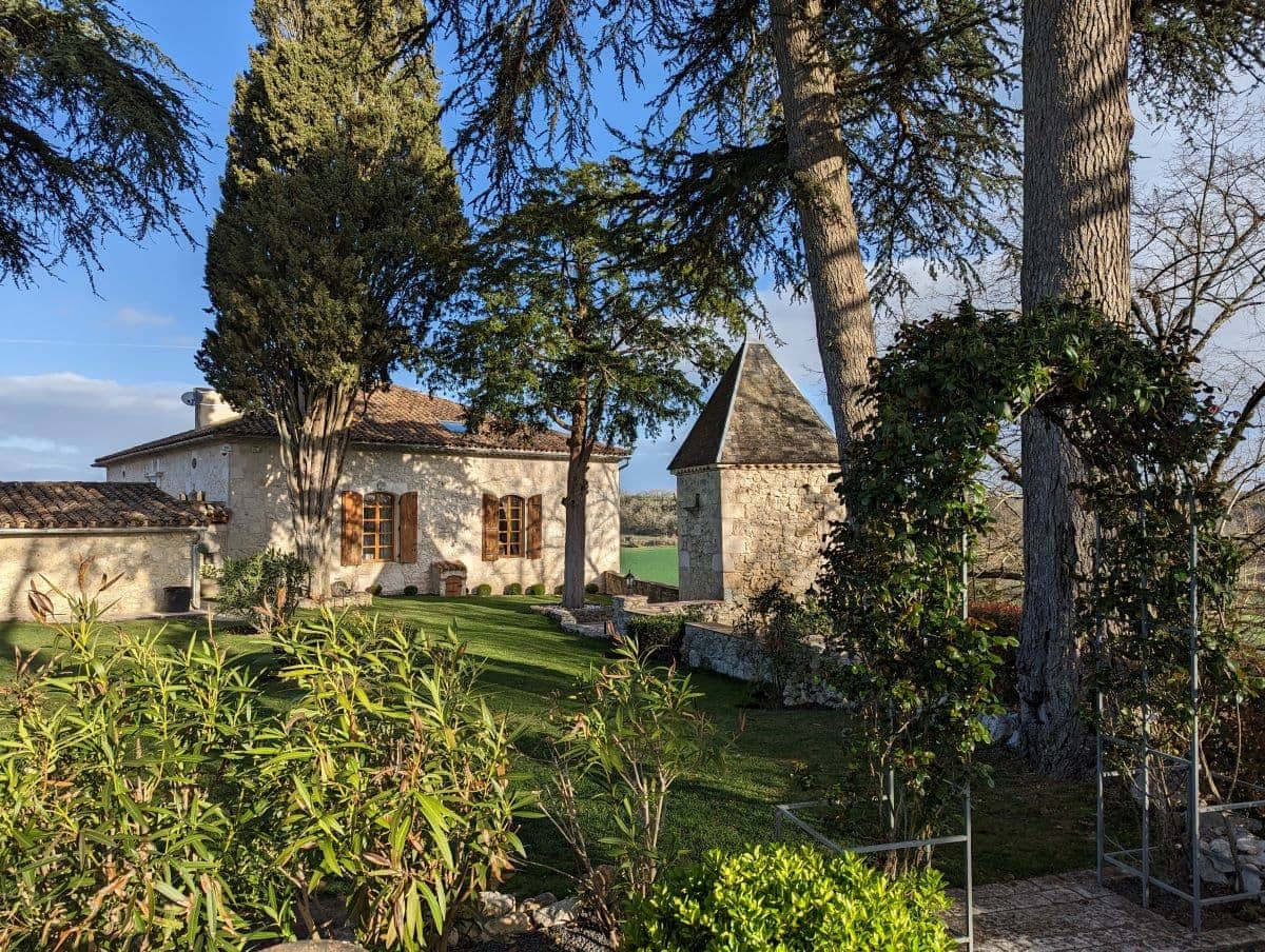 A Chateau in France that we housesit. A gate out of flowers is leading in a big garden in front of the historic building, under a blue sky.