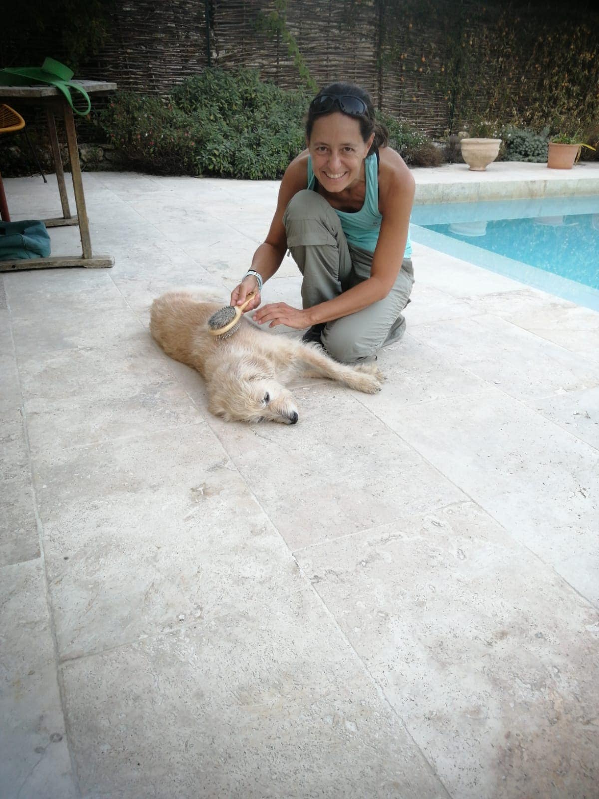 Linda sitzt neben einem Pool und bürstet einen entspannten, hellen Hund auf der Terrasse. Tierpflege gehört zum Alltag dazu, wenn man als Haussitter tätig ist.