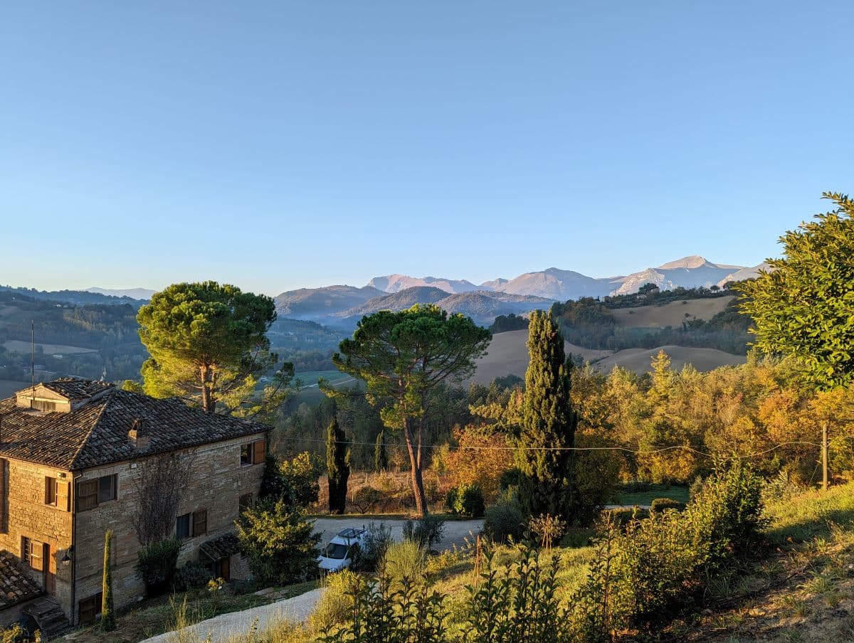 Large, old stone building with fantastic views. A driveway leads up to the house and in the background are high mountains with snow on them.
