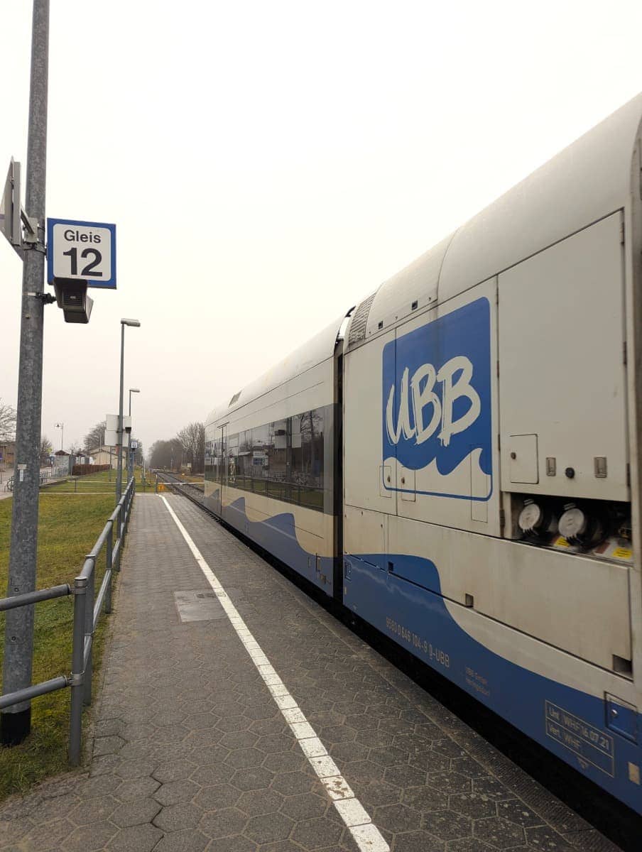 Ein UBB-Zug steht am Bahnsteig 12 eines kleinen Bahnhofs und ist abfahrbereit. Wenn Sie sich fragen, wie Sie nach Usedom kommen, ist die UBB-Bahn eine bequeme Möglichkeit, die Insel zu erreichen. Sie verbindet das Festland mit den Seebädern auf Usedom und bietet eine entspannte Fahrt durch die Küstenlandschaft.