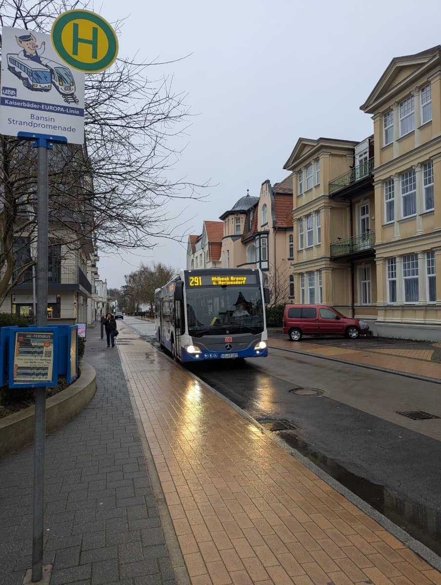 Ein Bus der Linie 291 hält an einem regnerischen Tag an der Haltestelle Bansin Strandpromenade, mit eleganten Villen am Meer im Hintergrund. Wenn Sie sich fragen, wie Sie nach Usedom kommen, bieten Busse wie dieser eine bequeme Verbindung zwischen den verschiedenen Orten der Insel, so dass Sie die Insel leicht ohne Auto erkunden können.