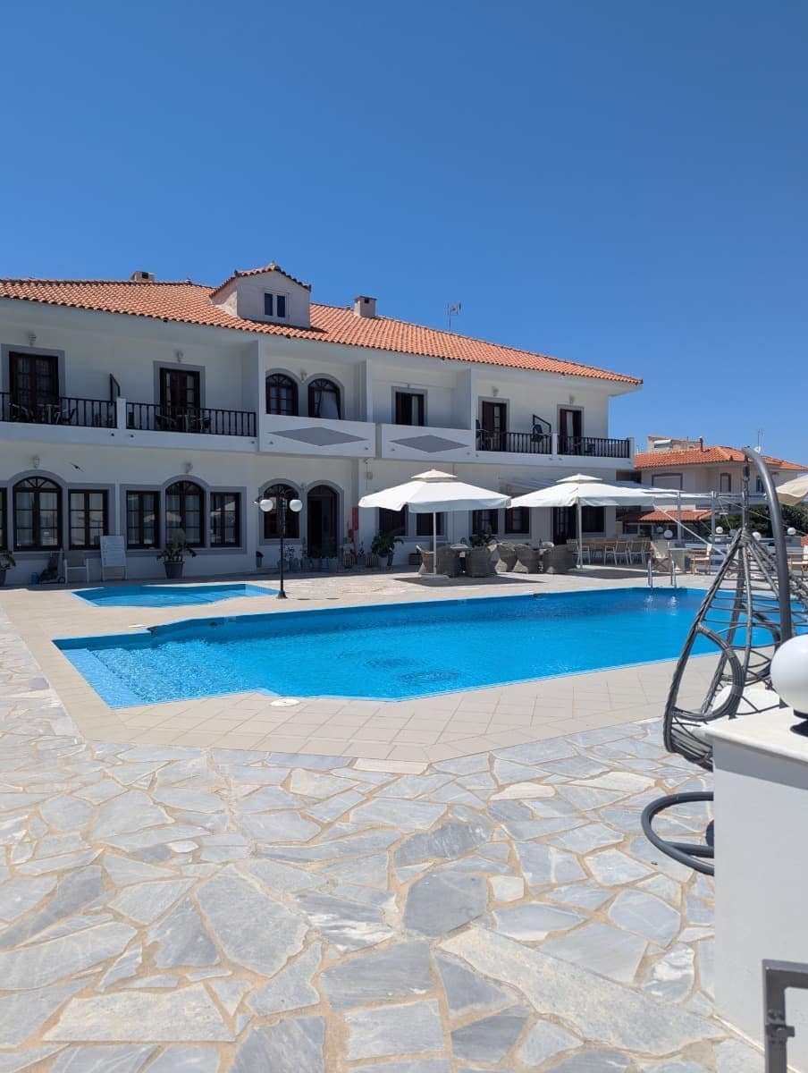 Die weiße Iro Residence mit ihrem gepflegten Poolbereich und mehreren Sonnenliegen spiegelt die Ruhe und Erholung im Samos Urlaub wider.