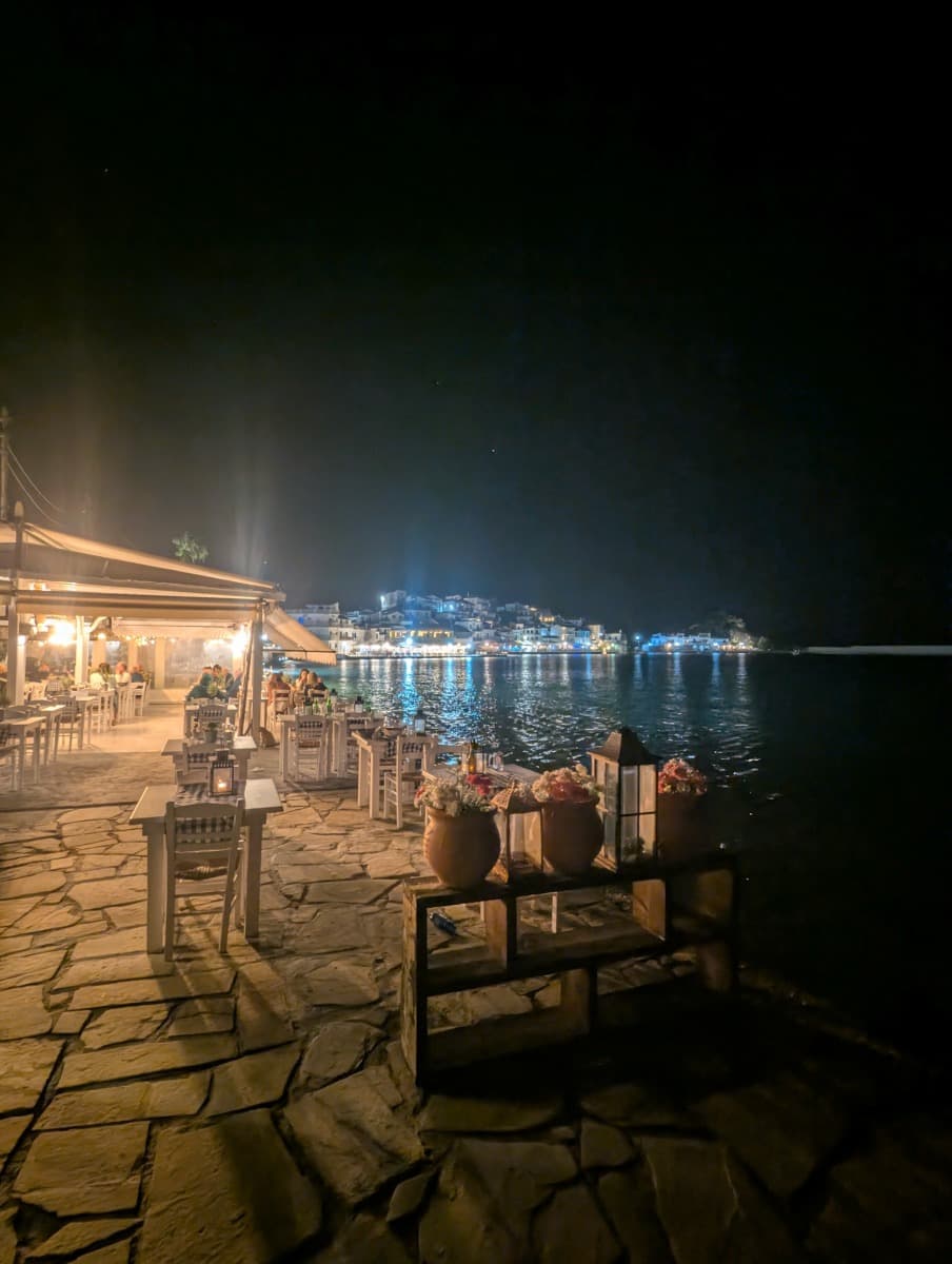 Beleuchtete Tavernen mit weißen Holzmöbeln säumen abends die Promenade direkt am Wasser, während sich die Lichter im Meer spiegeln. Die nächtliche Atmosphäre an der Promenade von Kokkari macht diesen Ort zu einer der stimmungsvollsten Samos Sehenswürdigkeiten.
