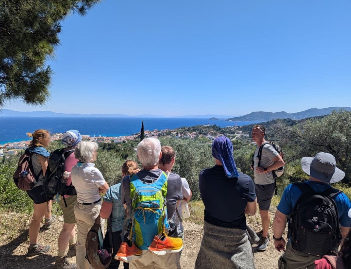 Eine Wandergruppe macht Halt mit Blick auf die türkisfarbene Küste und ein Küstendorf. Naturerlebnisse wie diese prägen den Urlaub auf Samos.
