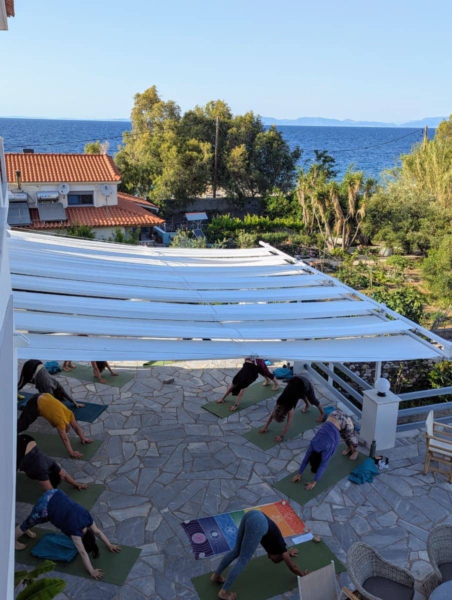 Eine Gruppe praktiziert Yoga auf einer schattigen Terrasse mit Meerblick – dieser entspannte Morgen ist typisch für den Urlaub auf Samos mit Froschreisen.