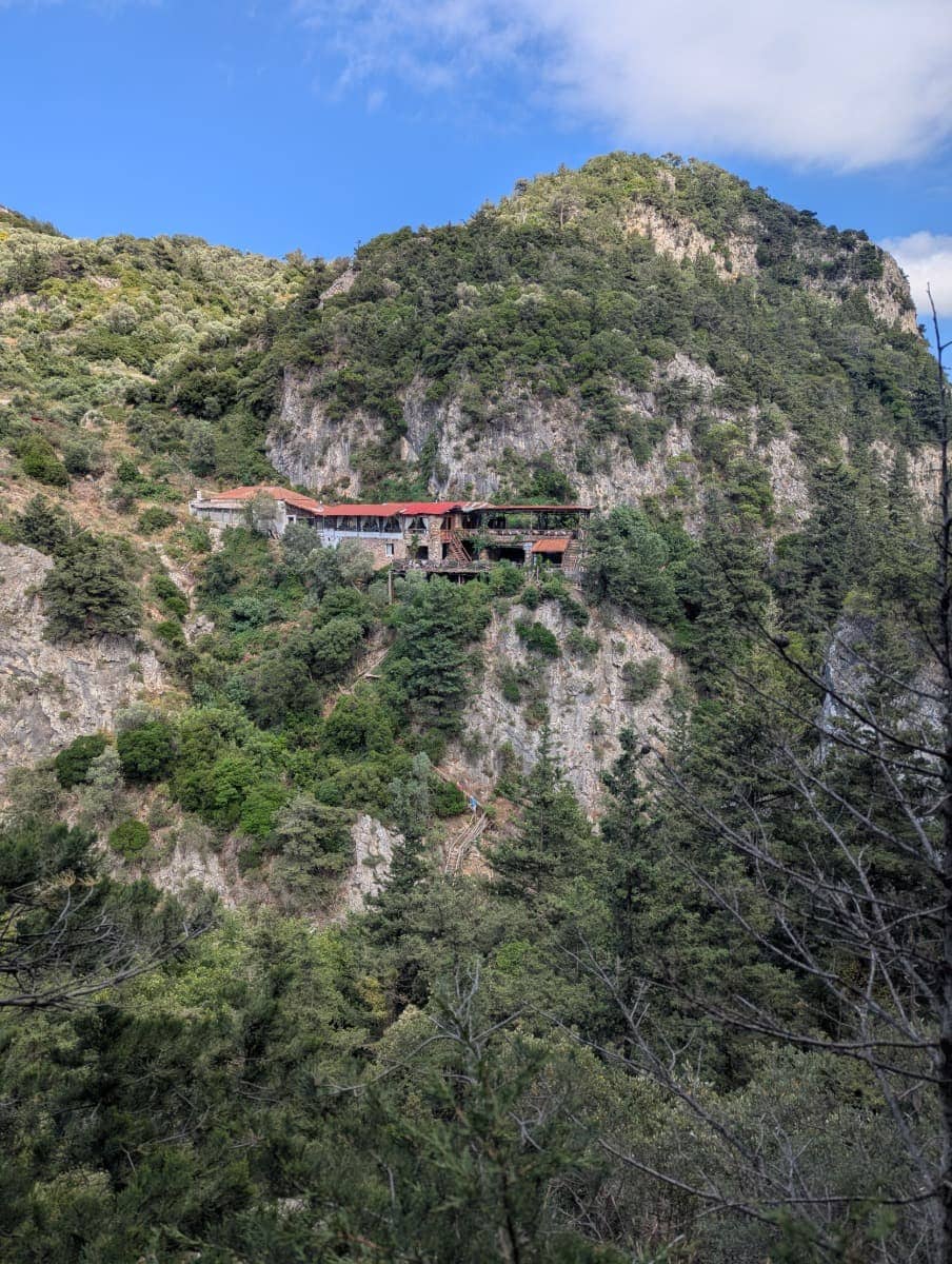 Die Taverne Archontissa liegt malerisch an einem steilen Hang über der Potami Schlucht auf Samos, mit Blick auf grüne Hügel und steile Felswände. Das Gebäude hebt sich in traditioneller Architektur von der umgebenden Natur ab.